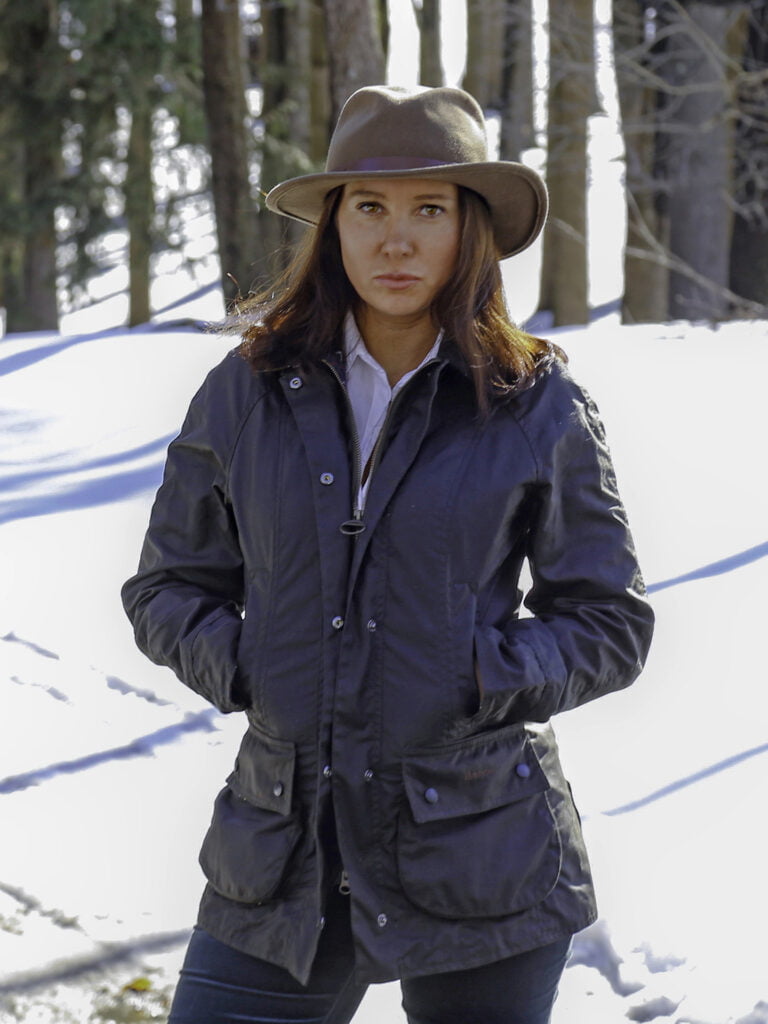 Kvinna med cowboyhatt som står i en snöig skog.