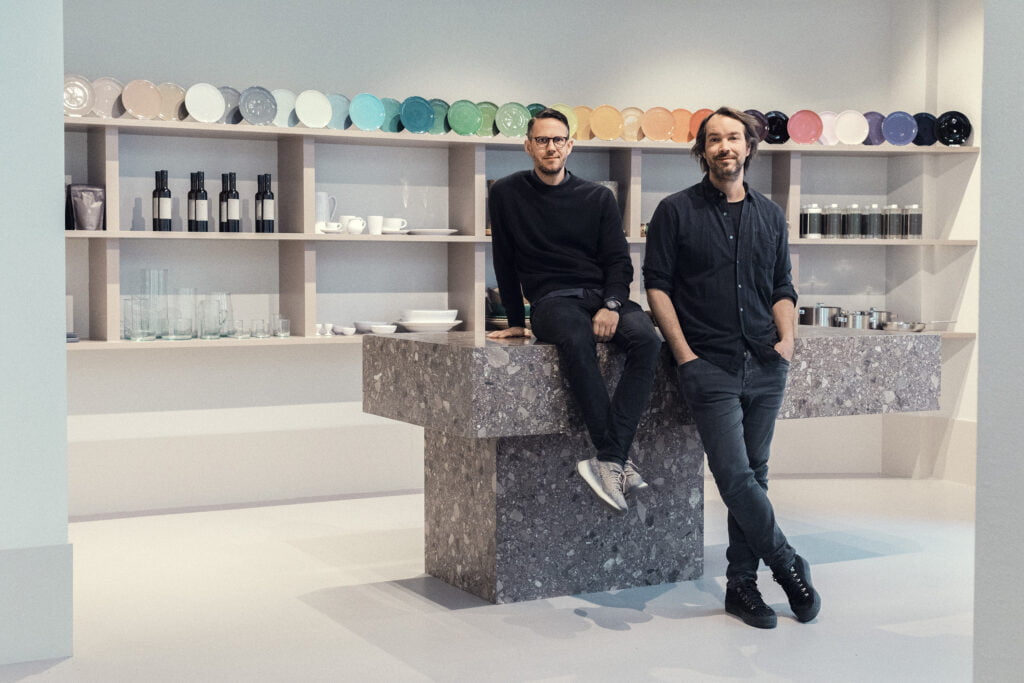 Två män som sitter i en butik med keramik, glas, flaskor m.m.